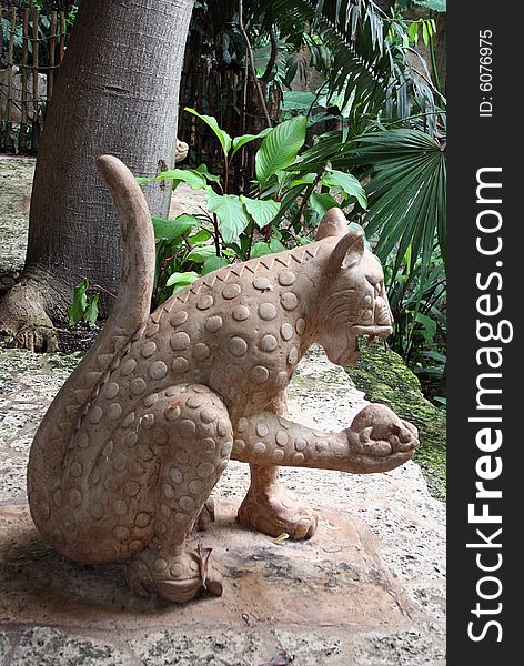 A jaguar statue stands among a tropical setting.