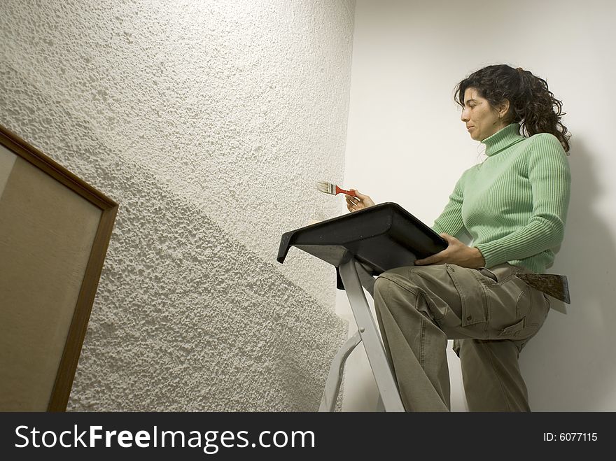 Woman paints a wall while standing on a ladder - Horizontally framed photo. Woman paints a wall while standing on a ladder - Horizontally framed photo