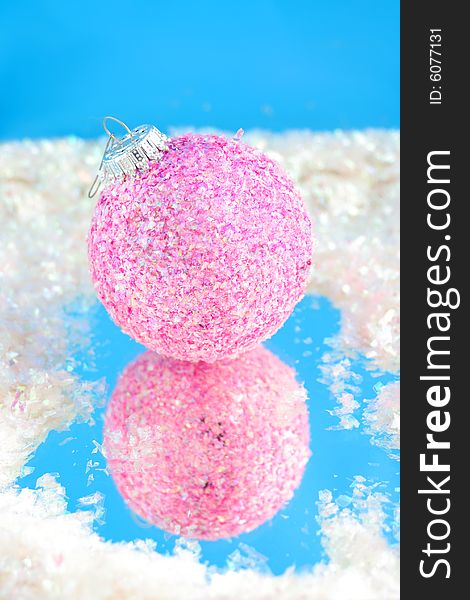 Pink sparkly christmas ball with reflection on blue surrounded by fake snow. Pink sparkly christmas ball with reflection on blue surrounded by fake snow