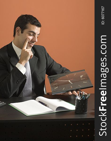 Business man smiles as he sits at his desk looking at his clock. Vertically framed photo. Business man smiles as he sits at his desk looking at his clock. Vertically framed photo.