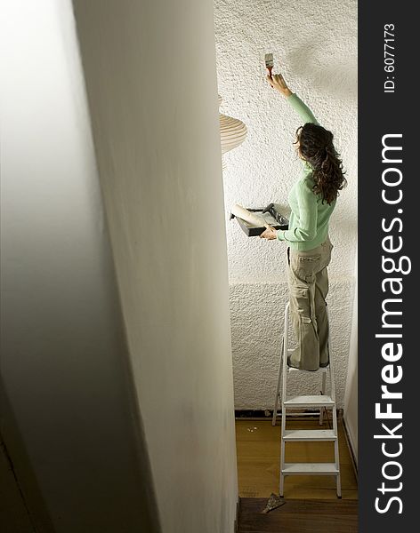 Woman paints a wall while standing on a ladder. Vertically framed photo. Woman paints a wall while standing on a ladder. Vertically framed photo.