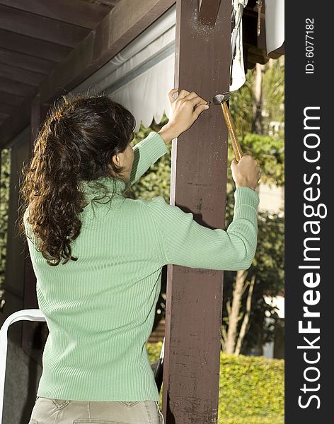 Woman hammers nail into post. Photo is taken from rear. Vertically framed photo. Woman hammers nail into post. Photo is taken from rear. Vertically framed photo.