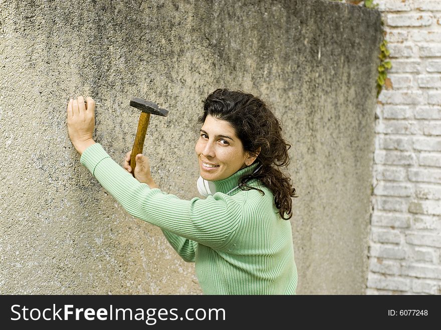 Woman smiling as she hammers a nail into a wall. Horizontally framed photo. Woman smiling as she hammers a nail into a wall. Horizontally framed photo.