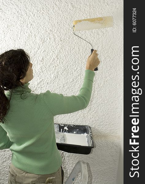 Woman uses a paint roller to paint a wall. Vertically framed photo. Woman uses a paint roller to paint a wall. Vertically framed photo.