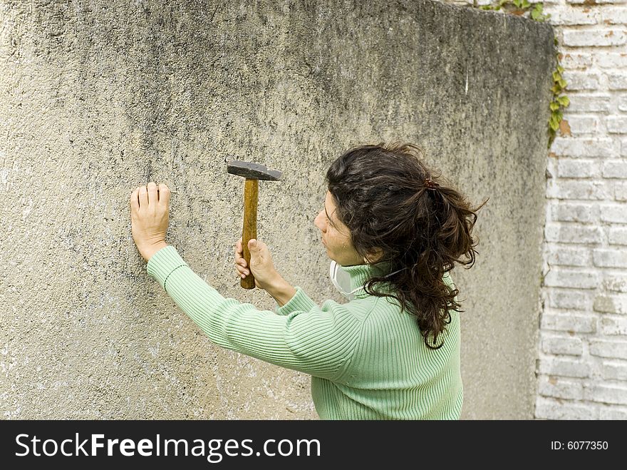 Woman hammers nail into wall. Horizontally framed photo. Woman hammers nail into wall. Horizontally framed photo.