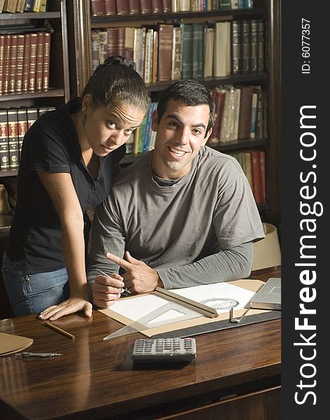 Couple studying books. He is smiling and she looks unhappy. There is a calculator, ruler, and protractors on the desk. Vertically framed photograph. Couple studying books. He is smiling and she looks unhappy. There is a calculator, ruler, and protractors on the desk. Vertically framed photograph.