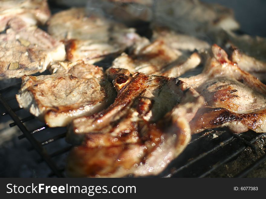 Roasted delicious pork steak being cooked on a grill outdoor. Roasted delicious pork steak being cooked on a grill outdoor.