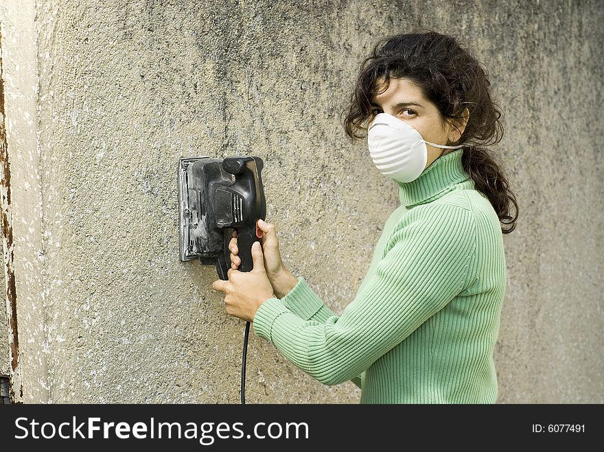 Woman wearing a mask using an electric sander. Horizontally framed photo. Woman wearing a mask using an electric sander. Horizontally framed photo.