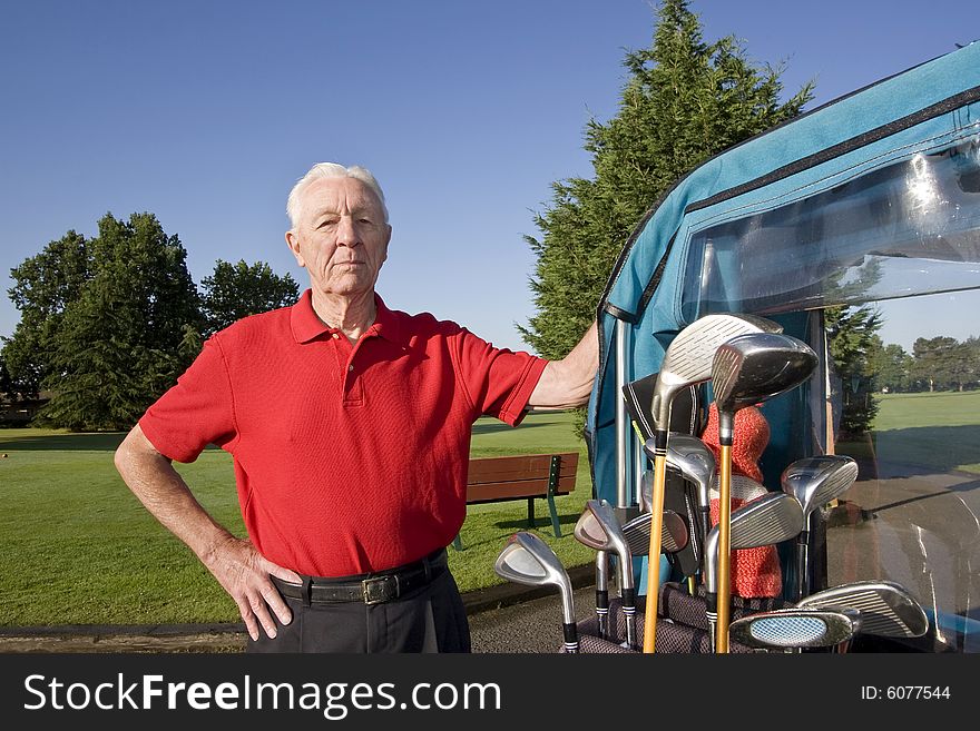 An elderly man is standing next to a golf cart on a golf course. He is smiling at the camera. Horizontally framed shot. An elderly man is standing next to a golf cart on a golf course. He is smiling at the camera. Horizontally framed shot.