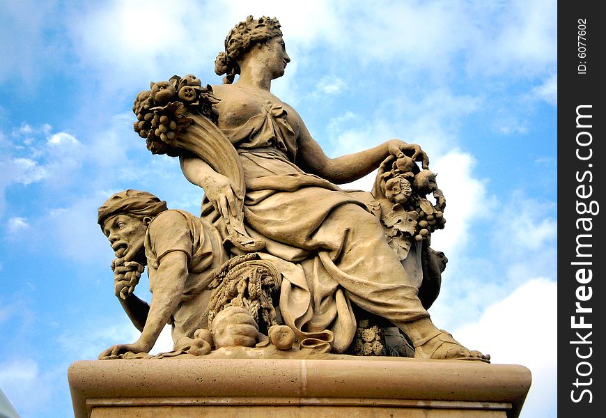 French sculpture of a woman holding cornucopia, surrounded by partially cloudy sky. French sculpture of a woman holding cornucopia, surrounded by partially cloudy sky.