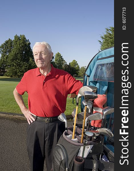 An elderly man is standing next to a golf cart on a golf course. He is smiling and looking away from the camera. Vertically framed shot. An elderly man is standing next to a golf cart on a golf course. He is smiling and looking away from the camera. Vertically framed shot.