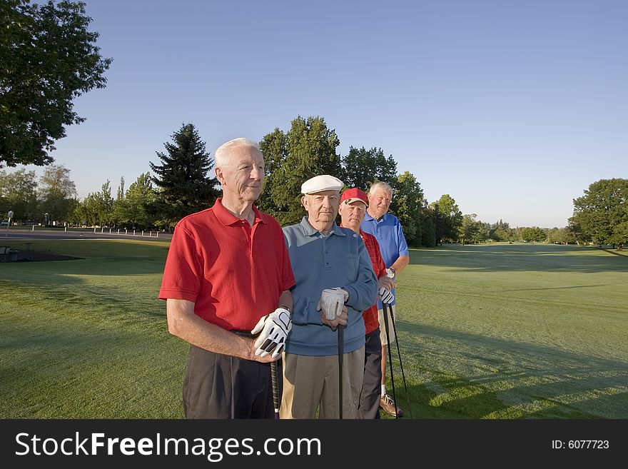Four elderly men are standing together on a golf course. They are holding their clubs, and some are smiling at the camera. Horizontally framed shot. Four elderly men are standing together on a golf course. They are holding their clubs, and some are smiling at the camera. Horizontally framed shot.