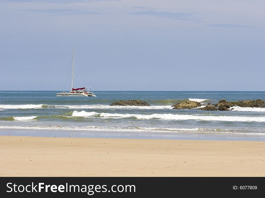 A nice catamaran anchored past the rocks off the coast. A nice catamaran anchored past the rocks off the coast