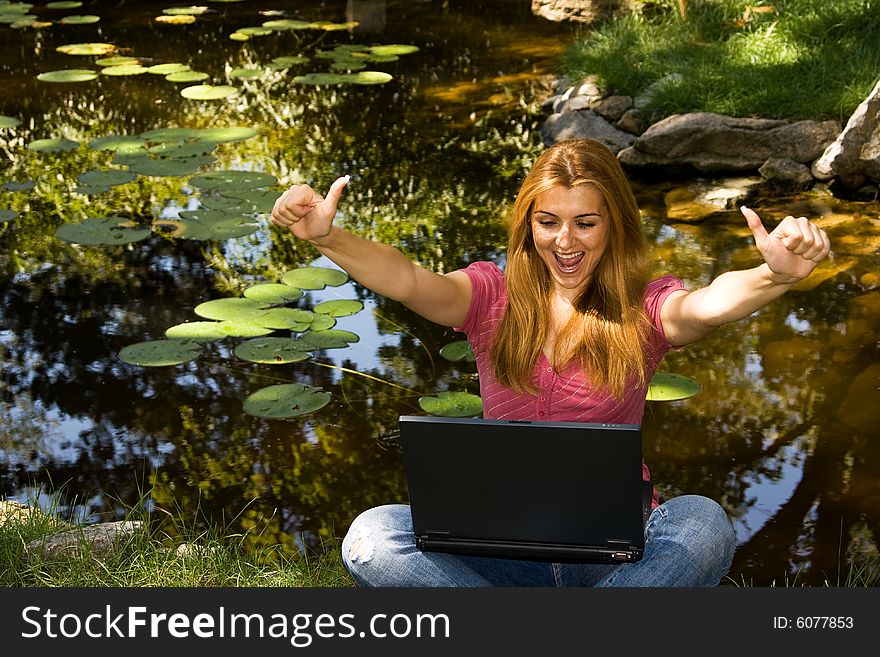 Happy beautiful student using laptop near water in park.