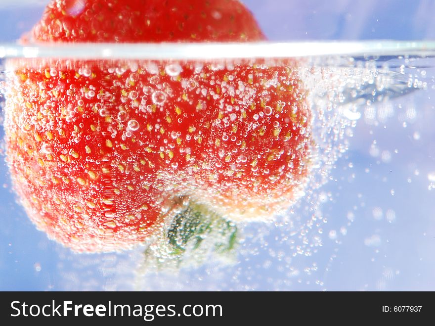 A fresh strawberry being submerged in water with bubbles. A fresh strawberry being submerged in water with bubbles.