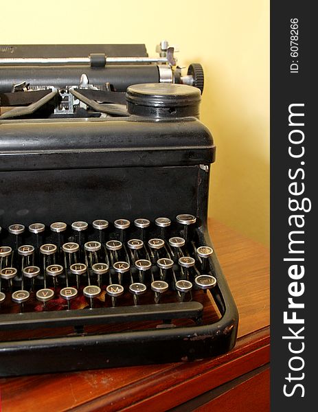 An antique typewriter sits on a wooden table against a yellow wall.