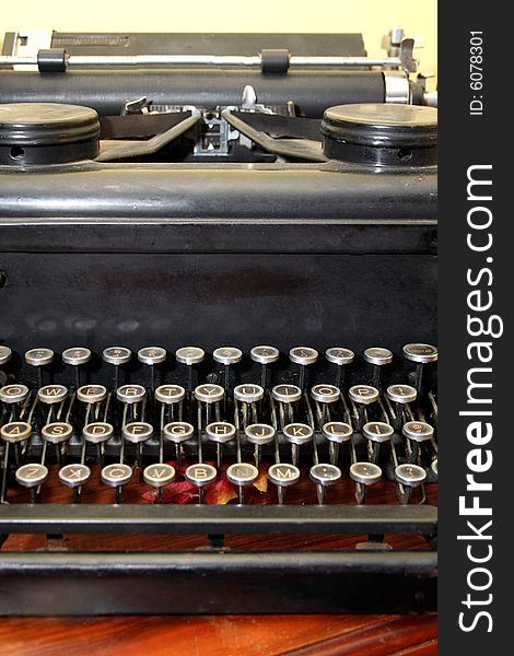 An antique typewriter sits on a wooden table against a yellow wall.