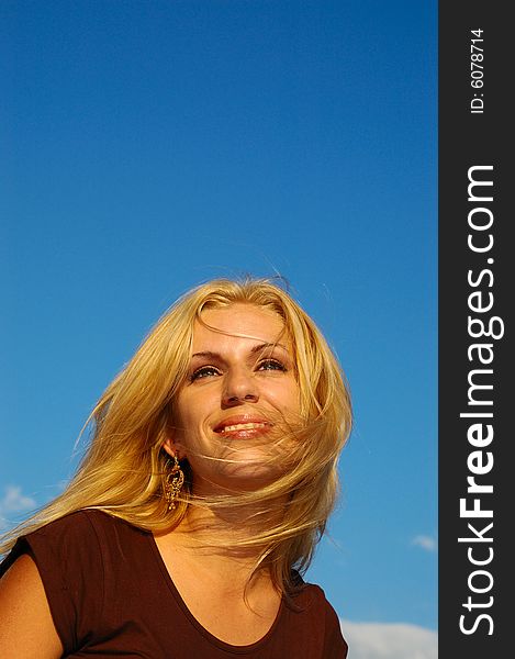 Smiling blond woman with fly-away hair against blue sky. Smiling blond woman with fly-away hair against blue sky