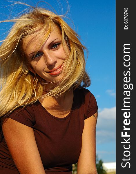Smiling blond woman with fly-away hair against blue sky. Smiling blond woman with fly-away hair against blue sky
