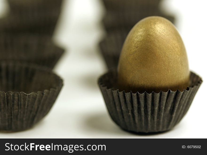 A golden egg inside a chocolate paper wrapper, blurred empty ones lined up in background and near