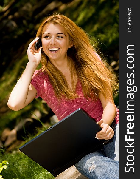 Happy young student using laptop and speaking by phone in natural environment. Happy young student using laptop and speaking by phone in natural environment.