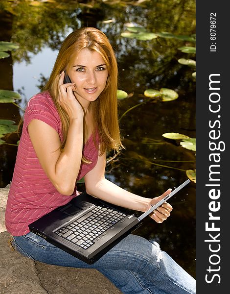 Happy young student using laptop and speaking by phone in natural environment. Happy young student using laptop and speaking by phone in natural environment.