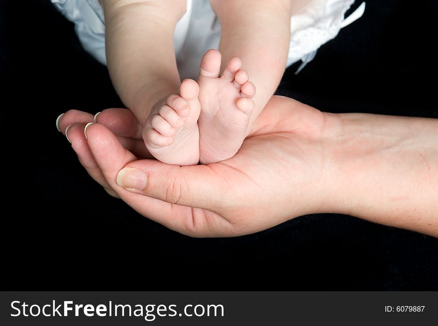 New born baby's feet supported in parent's hand shown on a black background. New born baby's feet supported in parent's hand shown on a black background.