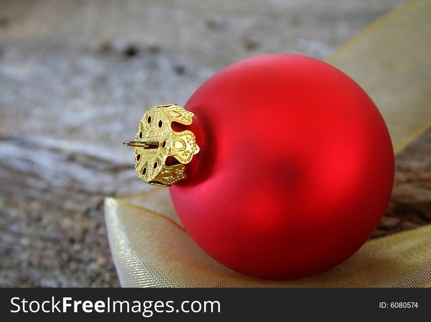 A single red Christmas ornament on a piece of gold ribbon and a wood textured background for the feel of a country Christmas.