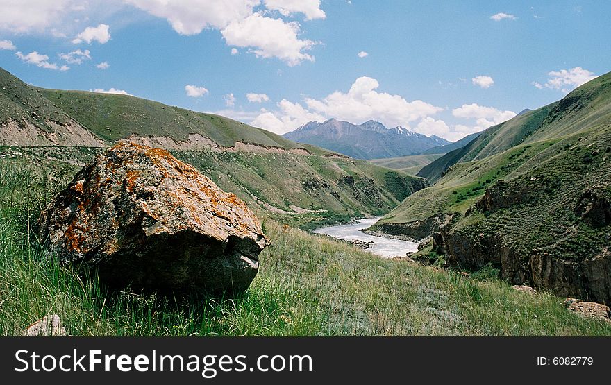 The big stone and the mountain river on a background of mountains and the blue sky. The big stone and the mountain river on a background of mountains and the blue sky