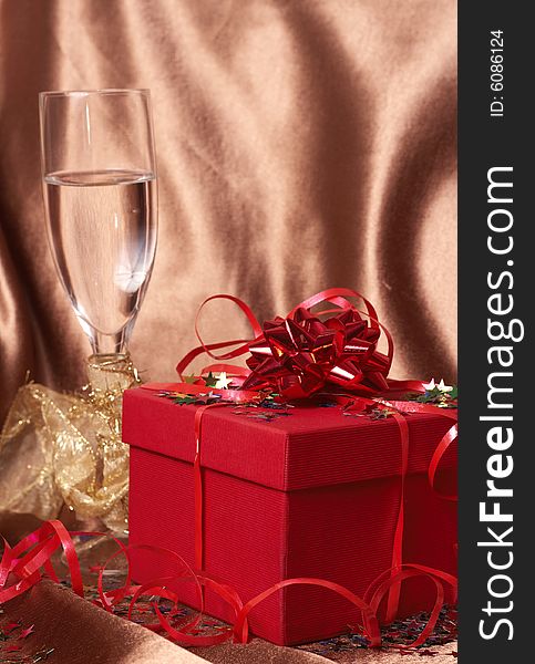 Party theme - red gift box with bows and stars with a glass of champagne on golden silk background