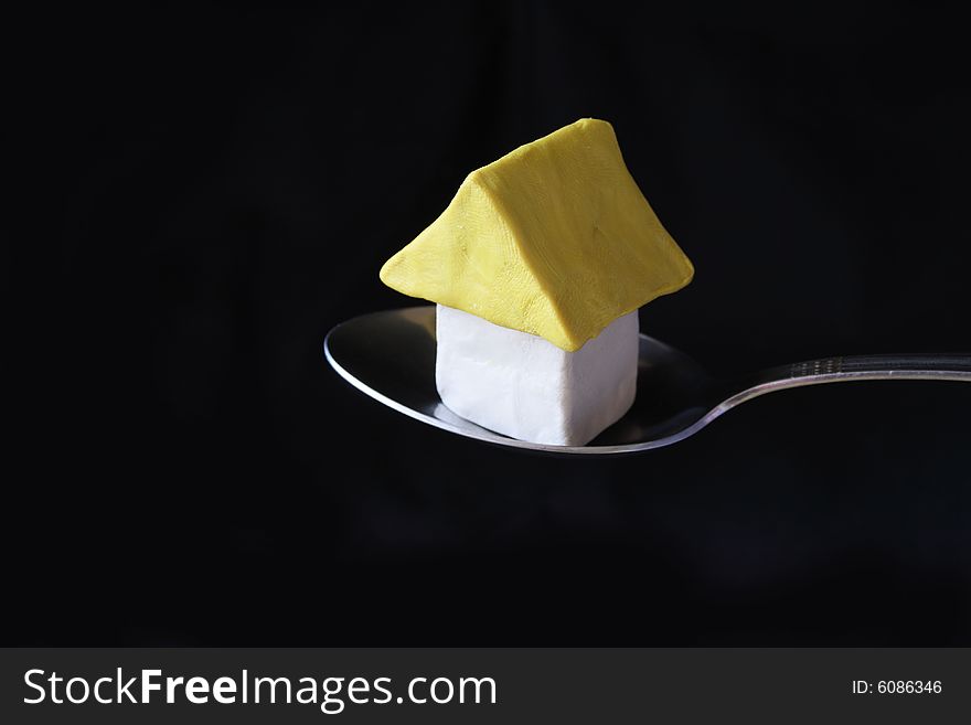 Little plasticine house in steel spoon on dark background. Little plasticine house in steel spoon on dark background