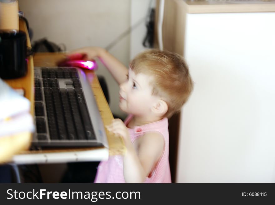 Little girl with hand on the computer's mouse looking at the display in motion blur. Little girl with hand on the computer's mouse looking at the display in motion blur