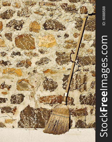 A rustic broom stick rests against a stone wall