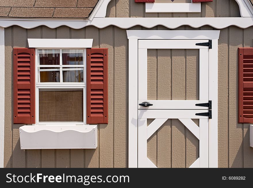 Closeup view of the front door and window to a small house or little cottage with window boxes and red shutters. Closeup view of the front door and window to a small house or little cottage with window boxes and red shutters.