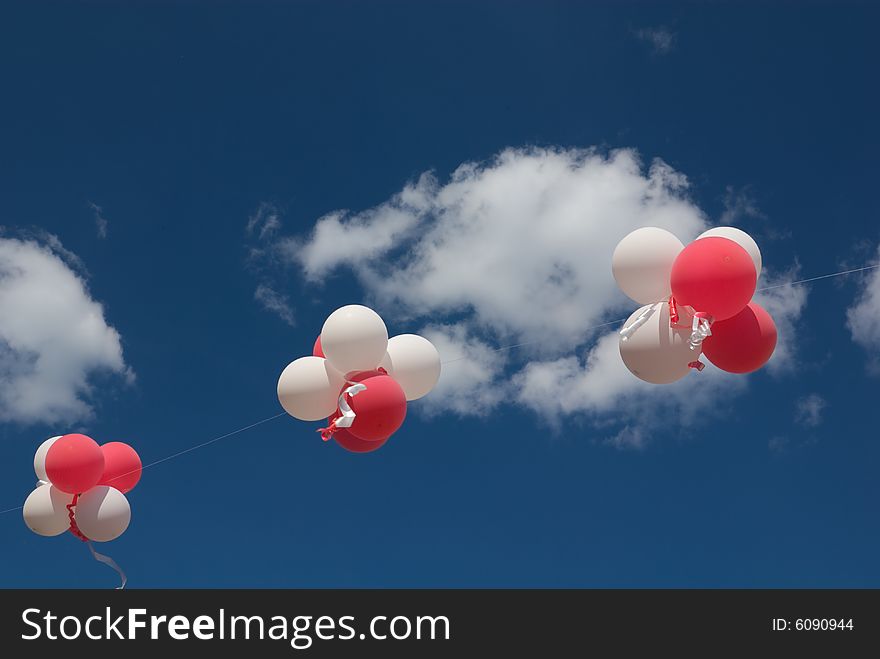 Red and white balloons with ribbons against blue sky.