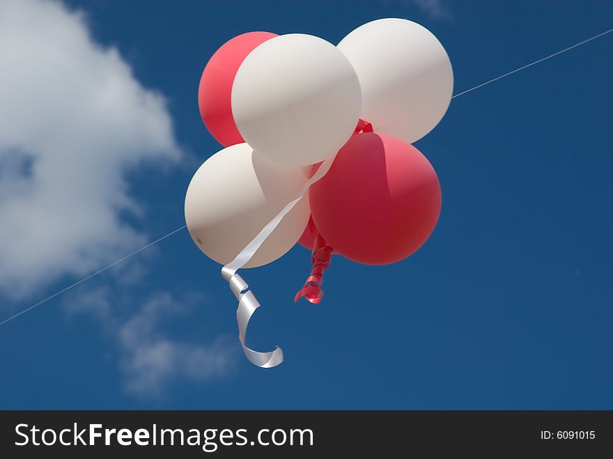 Red and white balloons with ribbons against blue sky.