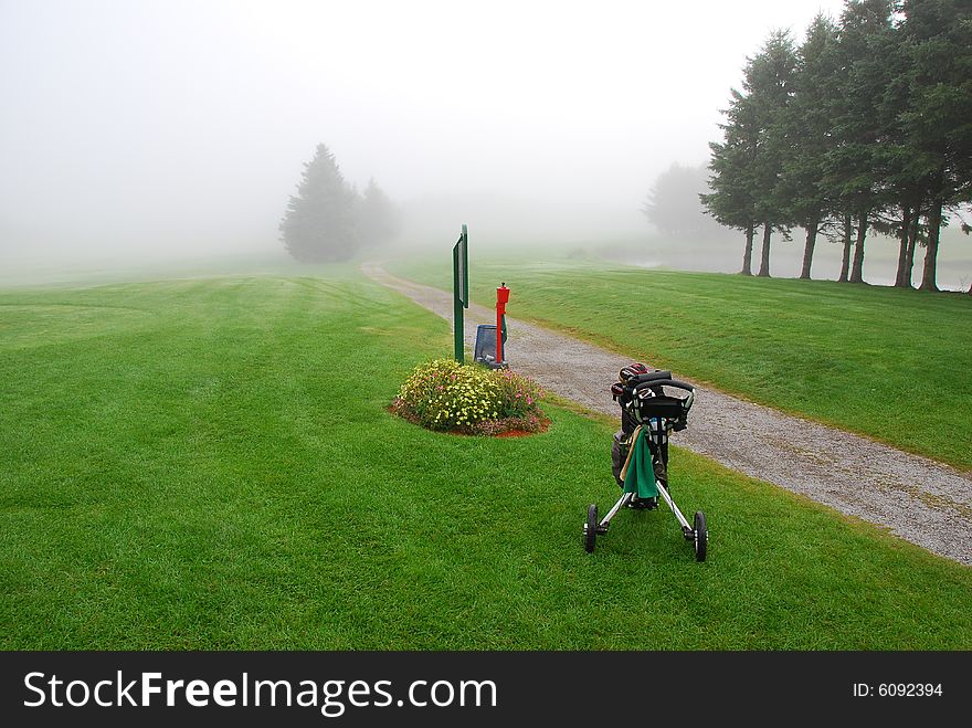 A golf bag and cart stand ready in the early morning fog. A golf bag and cart stand ready in the early morning fog.