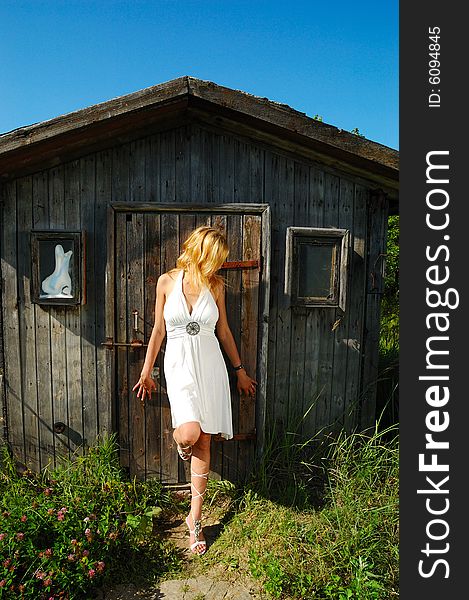 Blond woman in white dress standing near wood hut