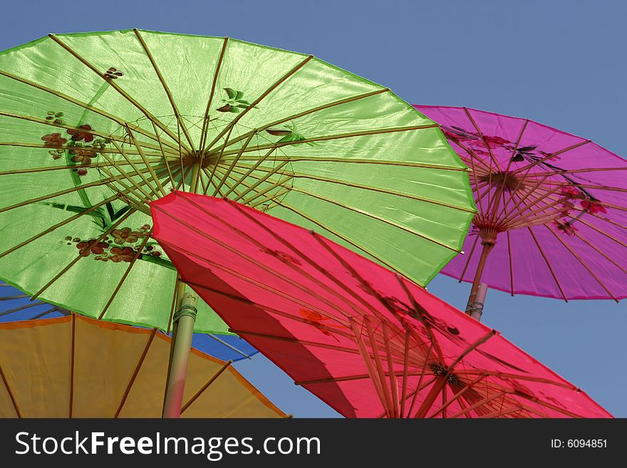 Colorful Asian-style paper parasols against a clear blue sky. Focus on center working of green parasol. Colorful Asian-style paper parasols against a clear blue sky. Focus on center working of green parasol.