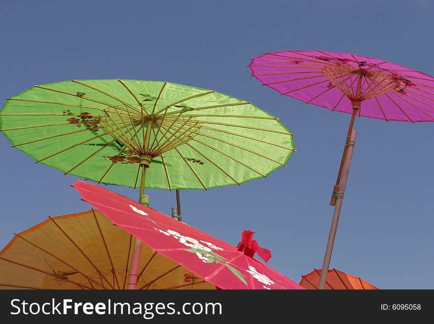 Colorful Asian-style paper parasols against a clear blue sky. Focus on center working of green parasol. Colorful Asian-style paper parasols against a clear blue sky. Focus on center working of green parasol.