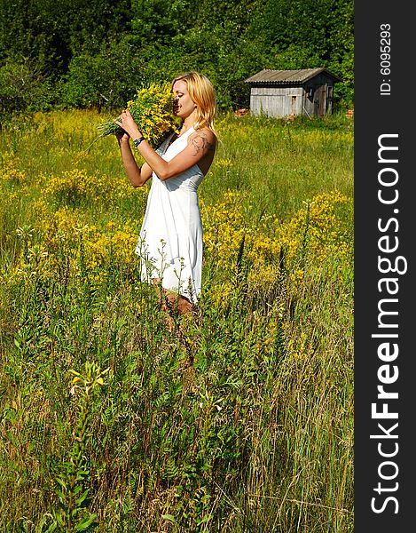 Blond woman in white dress smelling bunch of flowers. Blond woman in white dress smelling bunch of flowers