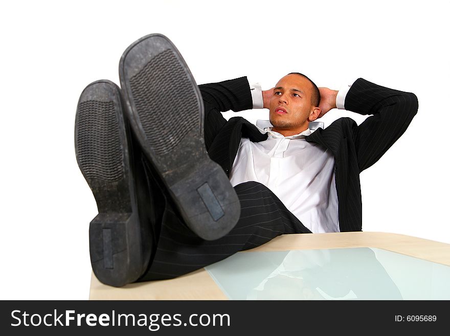 A young satisfied businessman sitting by desk at office feet on table thinking. A young satisfied businessman sitting by desk at office feet on table thinking.