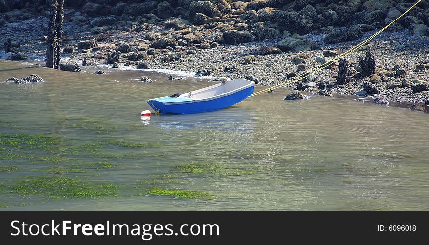 Rowboat anchored near the beach at low tide with a yellow rope running to shore. Rowboat anchored near the beach at low tide with a yellow rope running to shore.