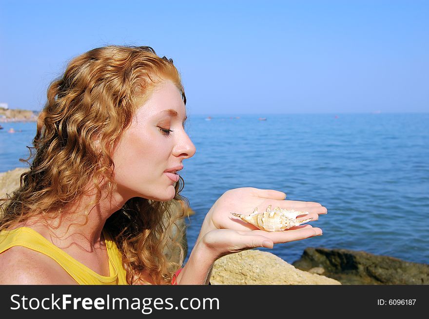 Beautiful girl holds a seashell in hands, sea background. Beautiful girl holds a seashell in hands, sea background