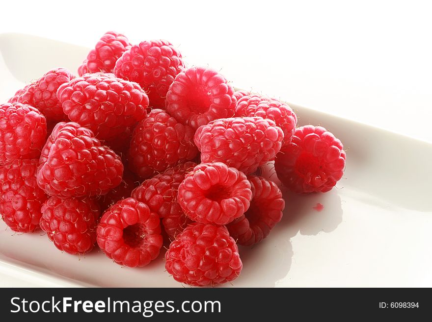 Pile of raspberries on a white dish, isolated on white. Pile of raspberries on a white dish, isolated on white