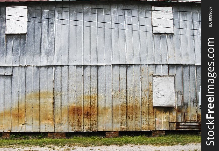 Metal barn covered in rust with broken window blocked in weather particle board. Metal barn covered in rust with broken window blocked in weather particle board.