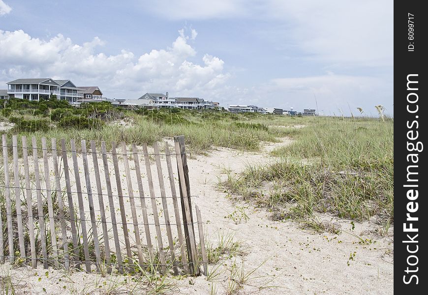 Wooden beach fence segregates the shore line beach from the large vacation homes. Wooden beach fence segregates the shore line beach from the large vacation homes.