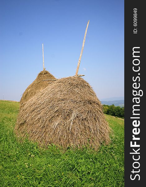 Two haystacks on a background of the blue sky and green grass