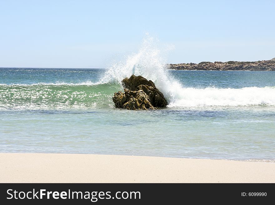 A wave crashing over a large rock in the summer time. A wave crashing over a large rock in the summer time