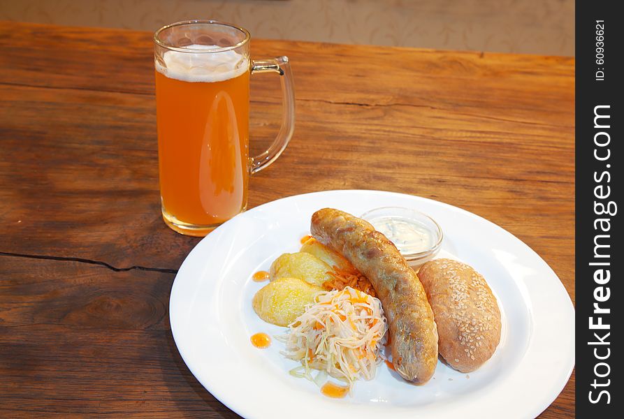 Fresh sausages with vegetables and mug with beer on a plate closeup